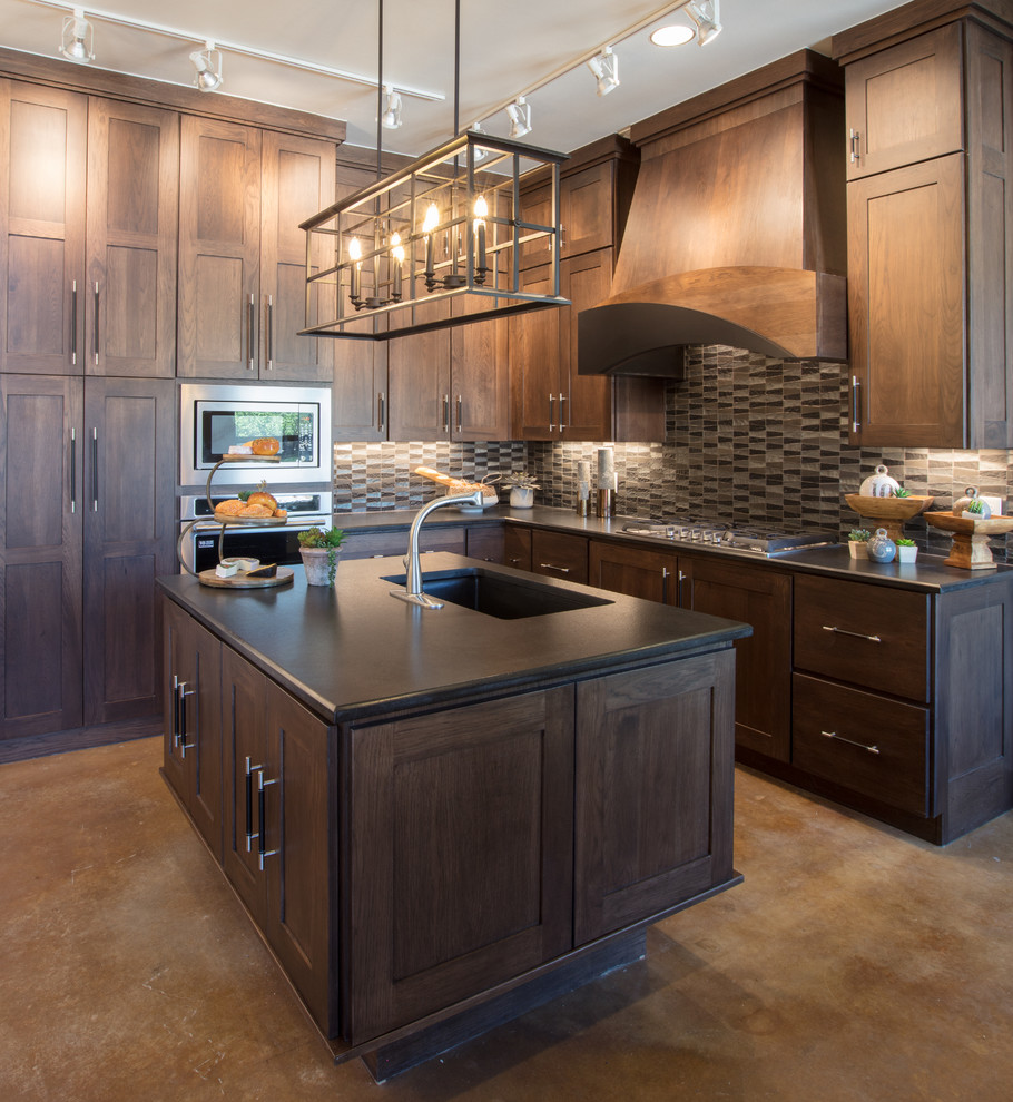 Mid-sized transitional l-shaped concrete floor and brown floor enclosed kitchen photo in Austin with an undermount sink, shaker cabinets, dark wood cabinets, granite countertops, multicolored backsplash, mosaic tile backsplash, stainless steel appliances, an island and black countertops