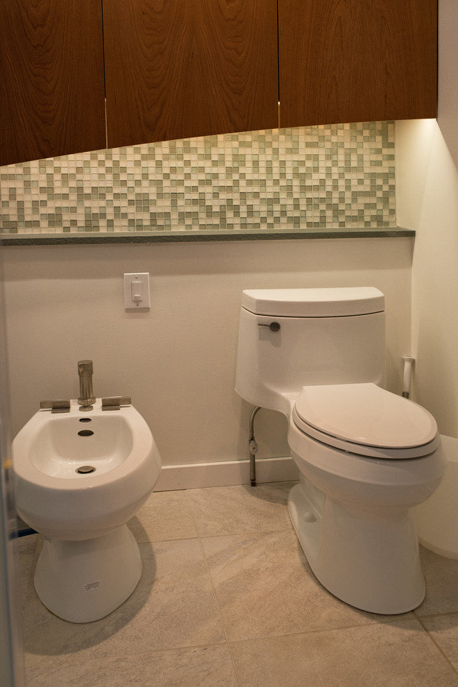 Inspiration for an expansive modern powder room in Philadelphia with flat-panel cabinets, medium wood cabinets, a one-piece toilet, black tile, pebble tile, white walls, ceramic floors, an undermount sink, granite benchtops and grey floor.