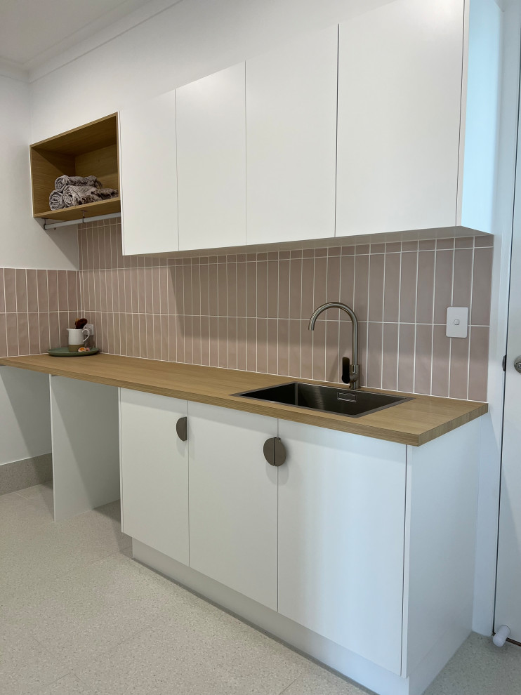 Mid-sized contemporary galley dedicated laundry room in Sunshine Coast with a drop-in sink, flat-panel cabinets, white cabinets, laminate benchtops, pink splashback, ceramic splashback, ceramic floors, a side-by-side washer and dryer, multi-coloured floor and brown benchtop.