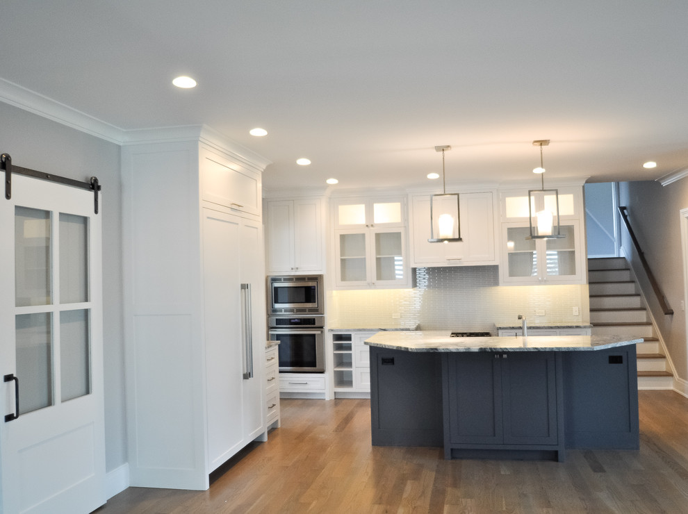 Inspiration for a mid-sized transitional l-shaped eat-in kitchen in New York with an undermount sink, shaker cabinets, white cabinets, granite benchtops, white splashback, ceramic splashback, panelled appliances, dark hardwood floors, with island, multi-coloured floor and grey benchtop.