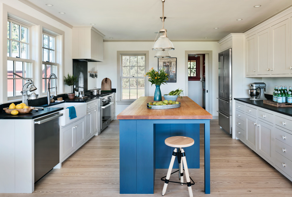 Design ideas for a traditional kitchen in New York with a farmhouse sink, shaker cabinets, beige cabinets, wood benchtops, stainless steel appliances, light hardwood floors, with island and black splashback.