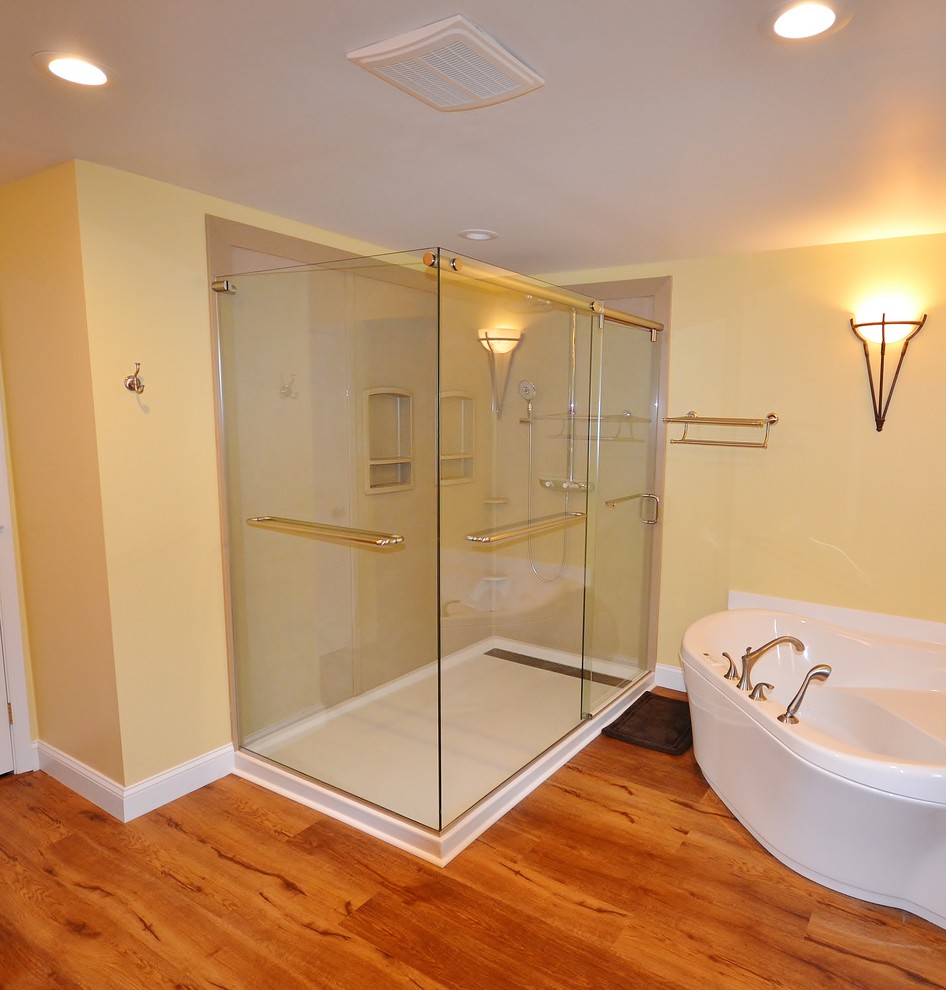 This is an example of a large transitional master bathroom in Philadelphia with raised-panel cabinets, medium wood cabinets, a corner tub, a corner shower, a two-piece toilet, yellow walls, laminate floors, an undermount sink, engineered quartz benchtops, brown floor, a sliding shower screen and brown benchtops.