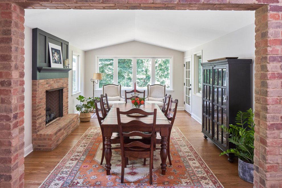 Mid-sized cottage medium tone wood floor, brown floor and vaulted ceiling kitchen/dining room combo photo in Charlotte with white walls, a standard fireplace and a brick fireplace