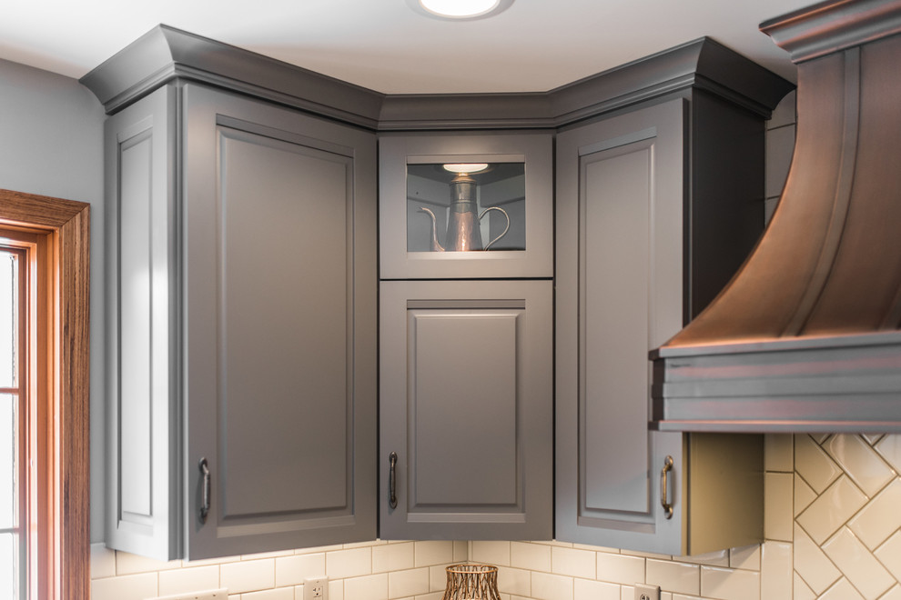 This is an example of a mid-sized traditional l-shaped eat-in kitchen in Chicago with an undermount sink, raised-panel cabinets, grey cabinets, quartz benchtops, white splashback, subway tile splashback, stainless steel appliances, light hardwood floors, a peninsula and multi-coloured benchtop.