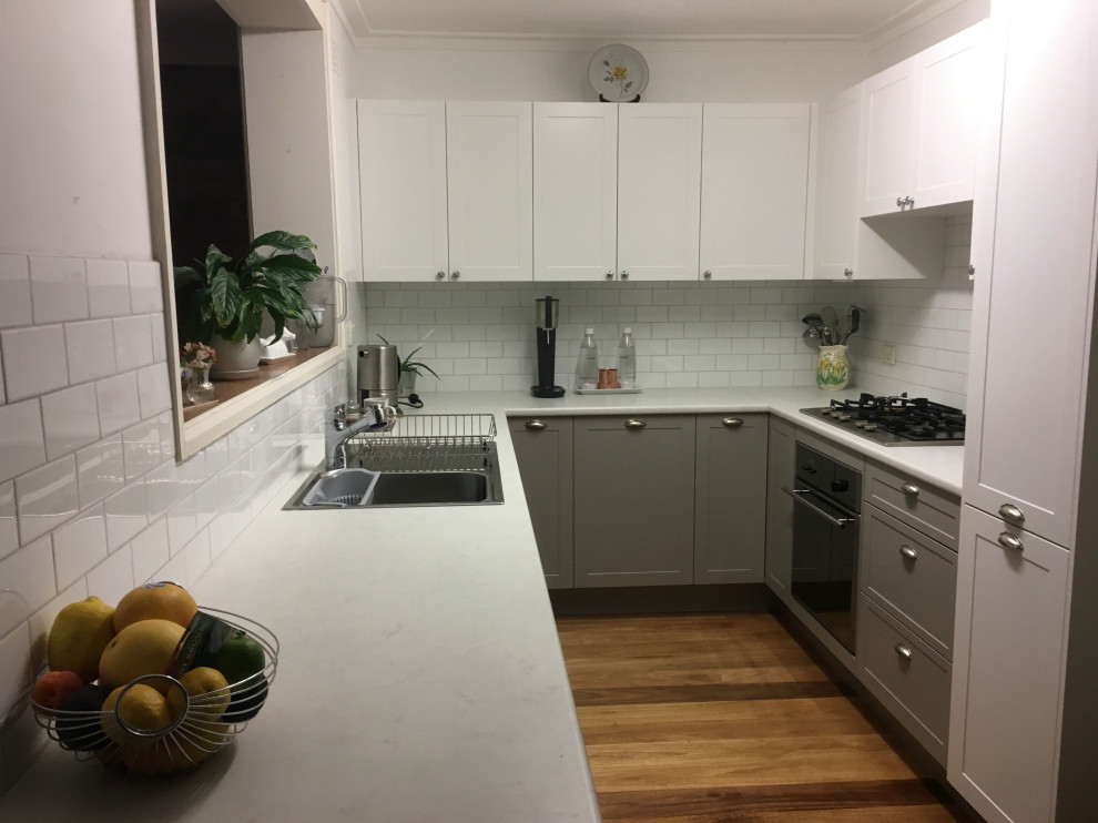 Inspiration for a small modern u-shaped kitchen pantry in Sydney with a built-in sink, white cabinets, laminate countertops, white splashback, ceramic splashback, stainless steel appliances, medium hardwood flooring, no island, brown floors and white worktops.