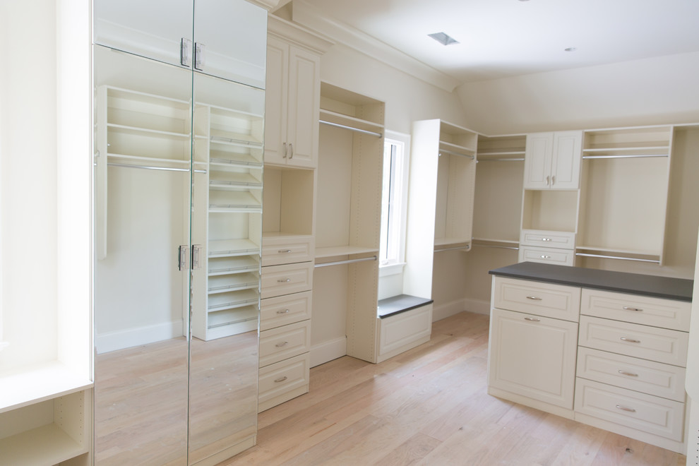 Large traditional gender-neutral walk-in wardrobe in Atlanta with raised-panel cabinets, white cabinets and light hardwood floors.