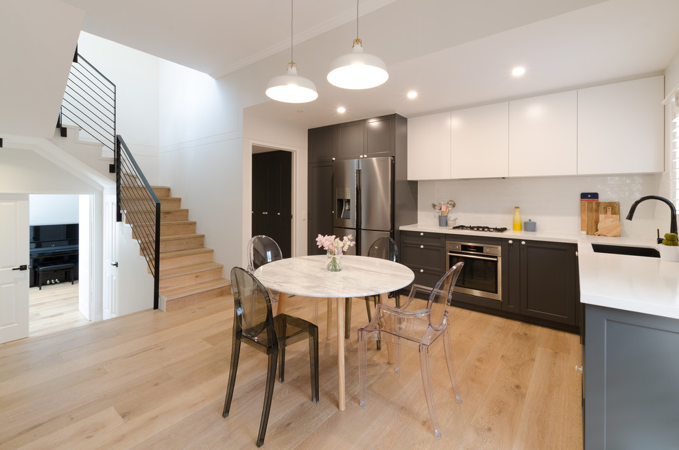 Photo of a mid-sized contemporary l-shaped eat-in kitchen in Sydney with a drop-in sink, shaker cabinets, grey cabinets, quartz benchtops, white splashback, subway tile splashback, stainless steel appliances, light hardwood floors and no island.