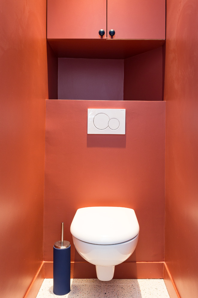 Photo of a small scandinavian powder room in London with a wall-mount toilet, flat-panel cabinets, red cabinets, red walls, terrazzo floors, white floor and white benchtops.