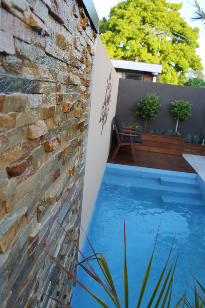 Mid-sized contemporary backyard rectangular lap pool in Melbourne with a water feature and natural stone pavers.