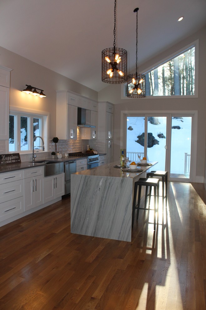 Eat-in kitchen - large transitional single-wall medium tone wood floor eat-in kitchen idea in Boston with a farmhouse sink, recessed-panel cabinets, white cabinets, quartz countertops, white backsplash, subway tile backsplash, stainless steel appliances and an island