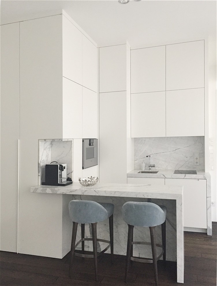 Small modern l-shaped open plan kitchen in Other with a drop-in sink, flat-panel cabinets, white cabinets, marble benchtops, multi-coloured splashback, stone slab splashback, black appliances, dark hardwood floors and grey benchtop.