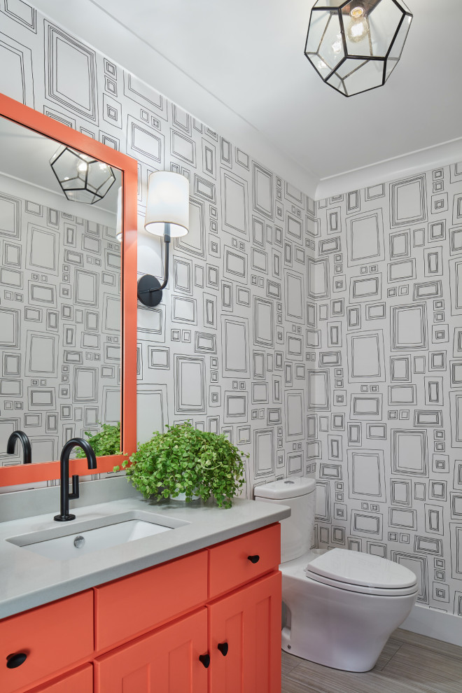 Inredning av ett klassiskt litet grå grått toalett, med orange skåp, en toalettstol med separat cisternkåpa, flerfärgade väggar och ett undermonterad handfat