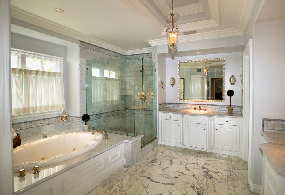 Photo of a traditional bathroom in Orange County with raised-panel cabinets, white cabinets, a drop-in tub, a corner shower, gray tile and marble.