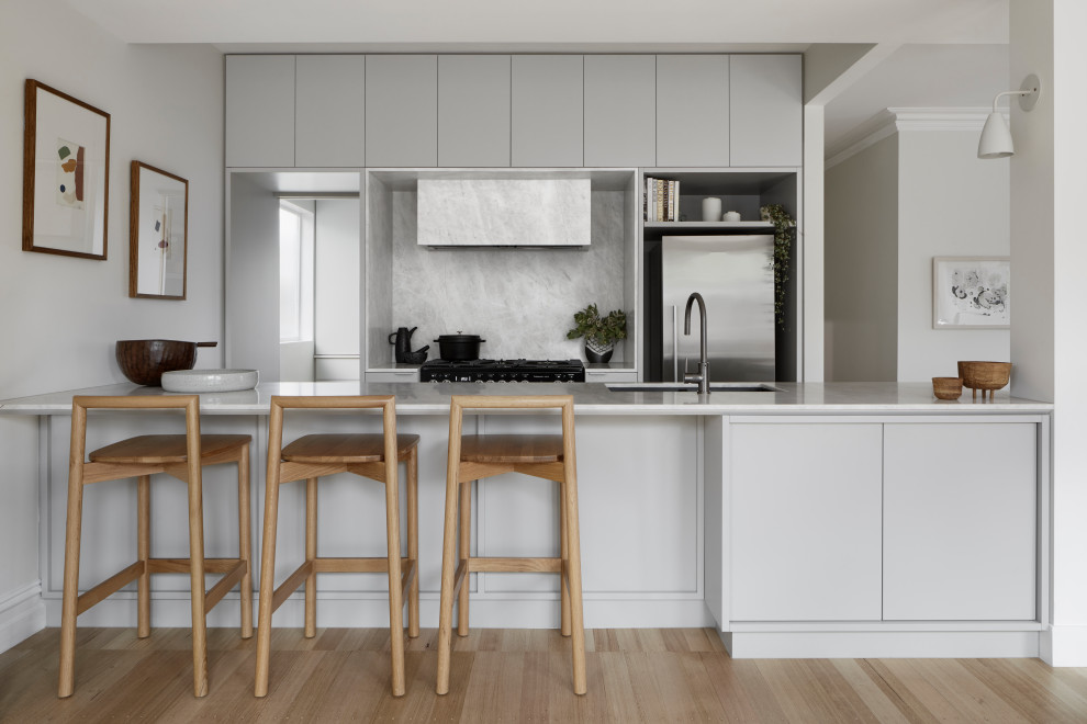 Small modern galley kitchen in Melbourne with grey cabinets, marble benchtops, grey splashback, marble splashback, stainless steel appliances, light hardwood floors, white benchtop, an undermount sink, flat-panel cabinets, a peninsula and beige floor.
