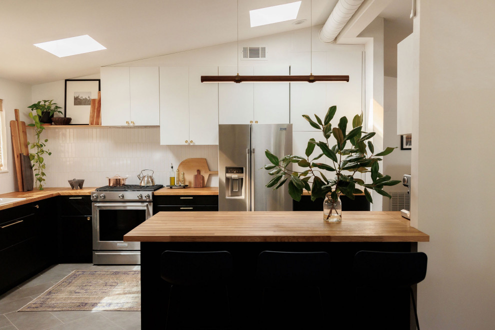 Midcentury l-shaped kitchen in Houston with a drop-in sink, flat-panel cabinets, black cabinets, wood benchtops, white splashback, stainless steel appliances, a peninsula, grey floor, brown benchtop and vaulted.