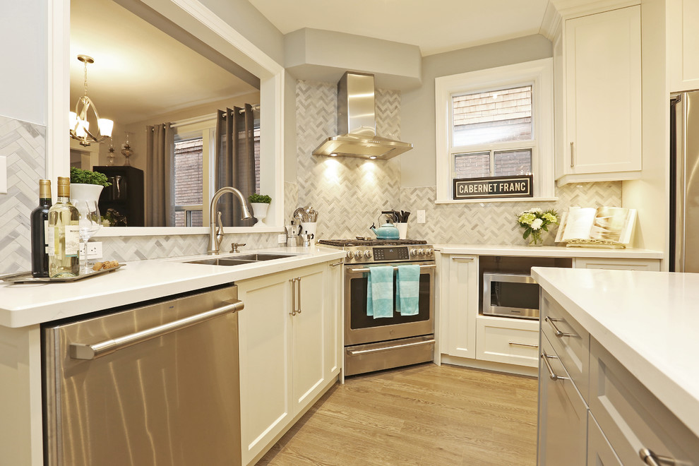 Enclosed kitchen - mid-sized transitional u-shaped light wood floor and brown floor enclosed kitchen idea in Toronto with an undermount sink, shaker cabinets, white cabinets, solid surface countertops, gray backsplash, stainless steel appliances, an island and white countertops