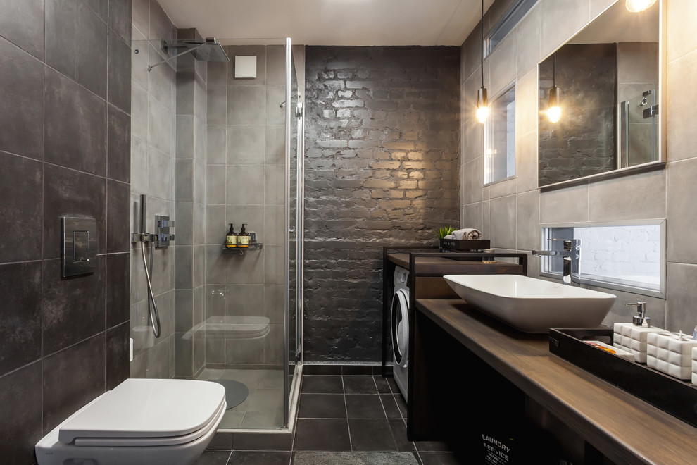 Mid-sized contemporary 3/4 bathroom in Other with gray tile, porcelain tile, black walls, ceramic floors, a vessel sink, wood benchtops, black floor, a hinged shower door, a corner shower, a wall-mount toilet and brown benchtops.