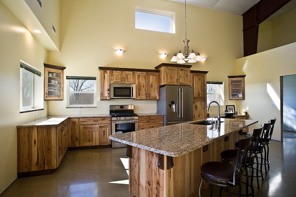 Mid-sized mountain style l-shaped concrete floor and brown floor eat-in kitchen photo with an undermount sink, shaker cabinets, light wood cabinets, granite countertops, stainless steel appliances and an island