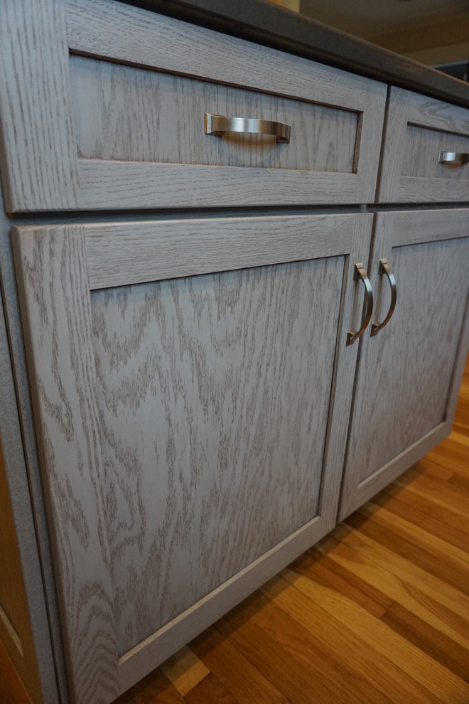 Mid-sized transitional u-shaped medium tone wood floor eat-in kitchen photo in Boston with an undermount sink, shaker cabinets, gray cabinets, quartz countertops, black backsplash, stainless steel appliances and an island