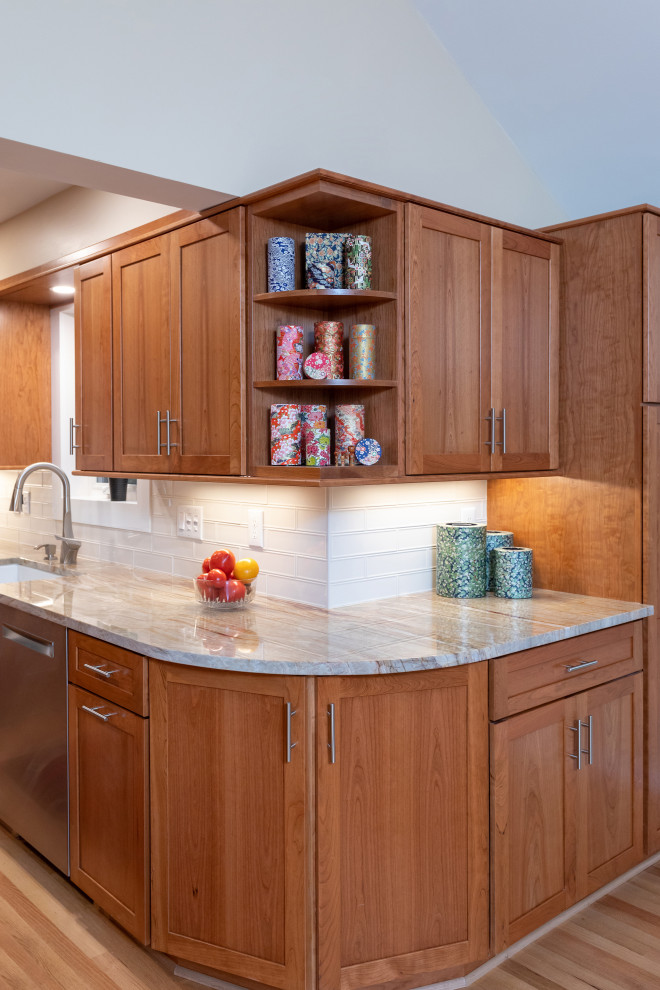 Mid-sized contemporary galley eat-in kitchen in Raleigh with a farmhouse sink, shaker cabinets, medium wood cabinets, granite benchtops, white splashback, porcelain splashback, stainless steel appliances, light hardwood floors, no island, brown floor, beige benchtop and vaulted.