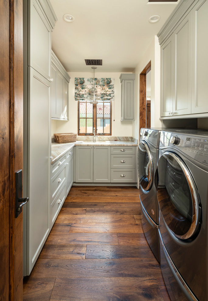 Design ideas for a traditional u-shaped dedicated laundry room in Phoenix with an undermount sink, recessed-panel cabinets, grey cabinets, medium hardwood floors, a side-by-side washer and dryer, brown floor, beige benchtop and white walls.
