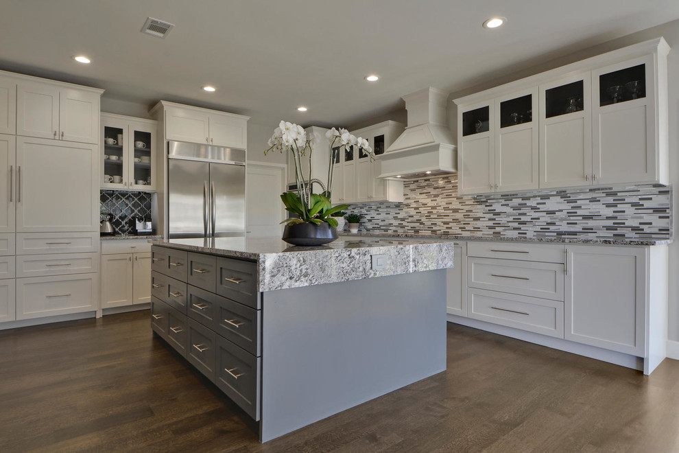 Example of a large transitional l-shaped dark wood floor enclosed kitchen design in Austin with an undermount sink, shaker cabinets, white cabinets, granite countertops, gray backsplash, mosaic tile backsplash, stainless steel appliances and an island