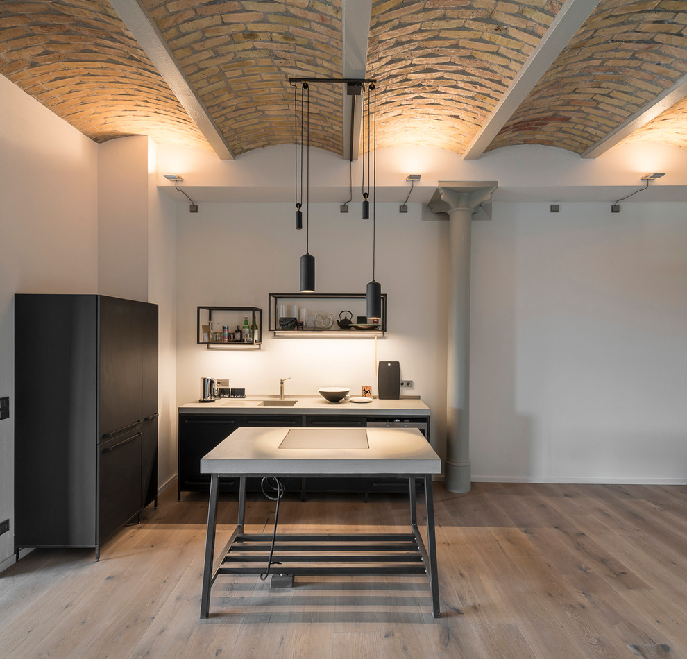 Inspiration for an expansive contemporary single-wall open plan kitchen in Berlin with an integrated sink, open cabinets, light hardwood floors, with island, concrete benchtops, white splashback, stainless steel appliances and black cabinets.