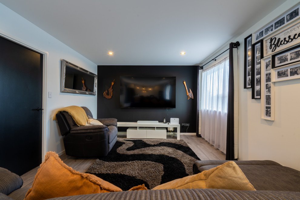 Ejemplo de cine en casa abierto actual de tamaño medio con paredes negras, suelo laminado, televisor colgado en la pared y suelo gris