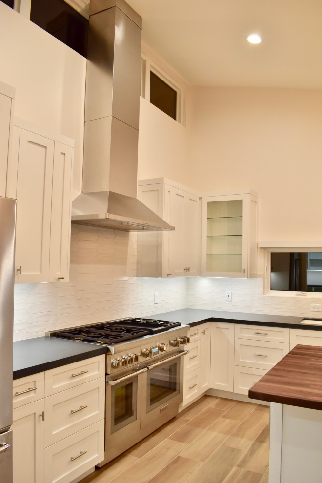 Large minimalist l-shaped eat-in kitchen photo with an undermount sink, shaker cabinets, white cabinets, quartz countertops, white backsplash, ceramic backsplash, stainless steel appliances, an island and black countertops