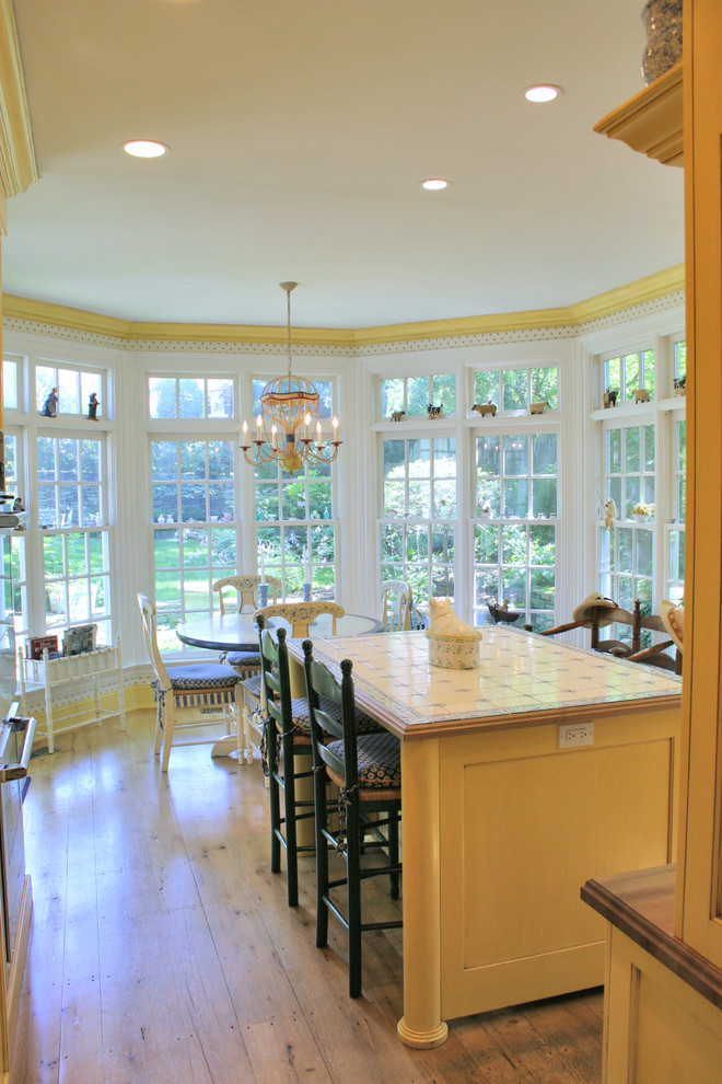 Photo of a mid-sized country eat-in kitchen in New York with recessed-panel cabinets, yellow cabinets, tile benchtops and with island.