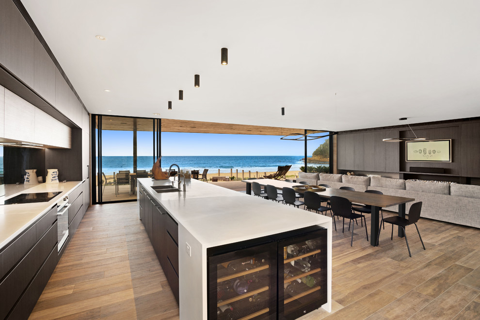Photo of an expansive contemporary galley open plan kitchen in Central Coast with flat-panel cabinets, dark wood cabinets, solid surface benchtops, black splashback, mirror splashback, black appliances, with island and white benchtop.
