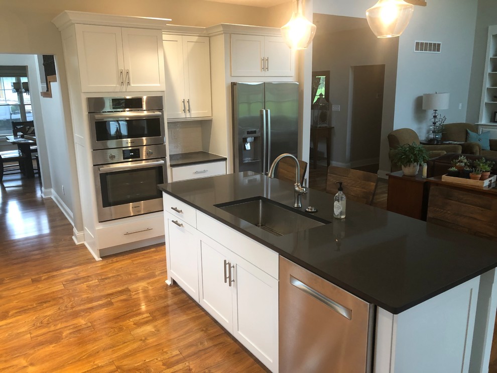 Kitchen - laminate floor and brown floor kitchen idea with a single-bowl sink, shaker cabinets, white cabinets, quartzite countertops, white backsplash, subway tile backsplash, stainless steel appliances, an island and gray countertops