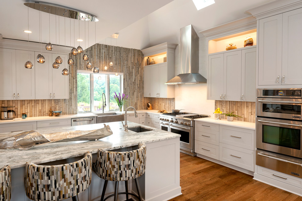 Transitional l-shaped medium tone wood floor kitchen photo with an undermount sink, shaker cabinets, beige cabinets, stainless steel appliances, an island and white countertops