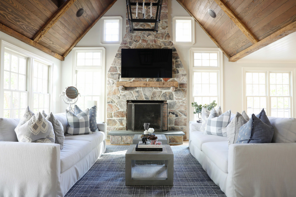 Large country open concept living room in New York with white walls, light hardwood floors, a stone fireplace surround, a wall-mounted tv, brown floor, wood and a standard fireplace.