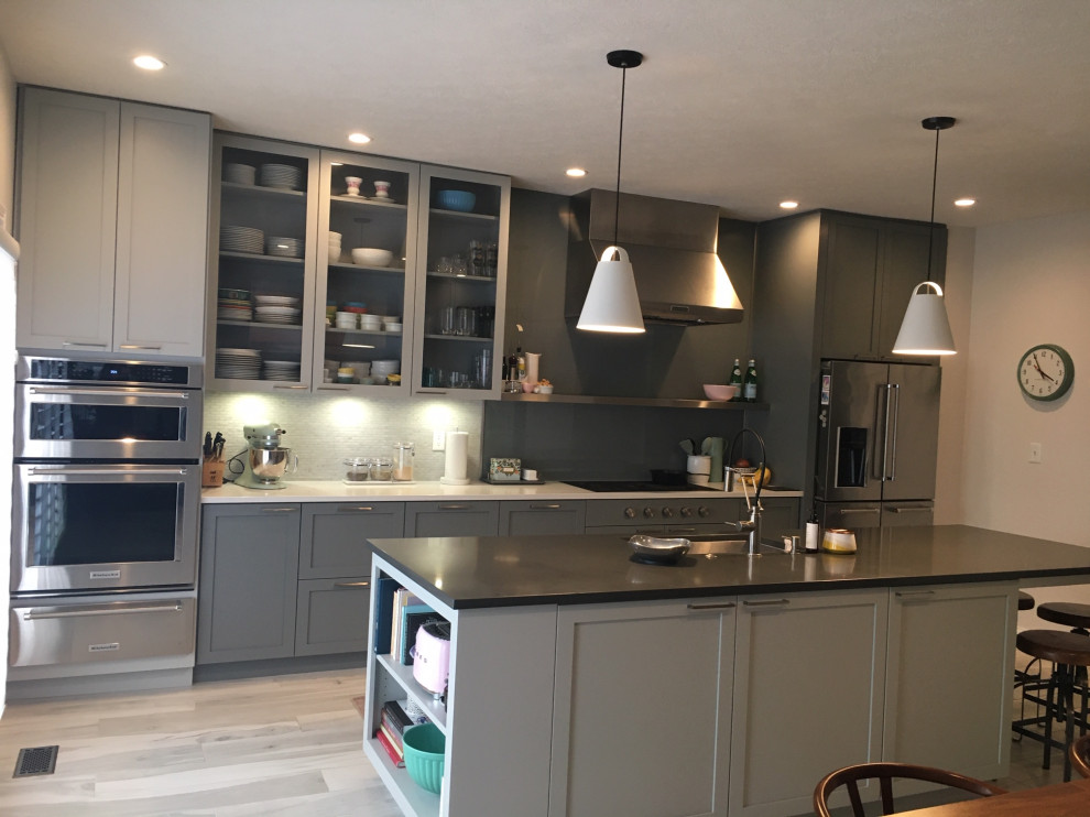 Photo of a mid-sized modern single-wall eat-in kitchen in Indianapolis with an undermount sink, recessed-panel cabinets, grey cabinets, quartz benchtops, grey splashback, glass sheet splashback, stainless steel appliances, porcelain floors, with island, grey floor and grey benchtop.