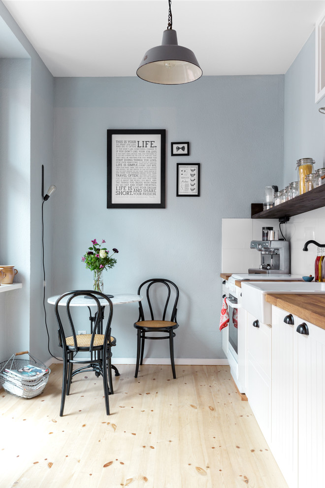 Inspiration for a small scandinavian single-wall eat-in kitchen in Berlin with a farmhouse sink, white cabinets, wood benchtops, white splashback, light hardwood floors, recessed-panel cabinets, white appliances, ceramic splashback and no island.