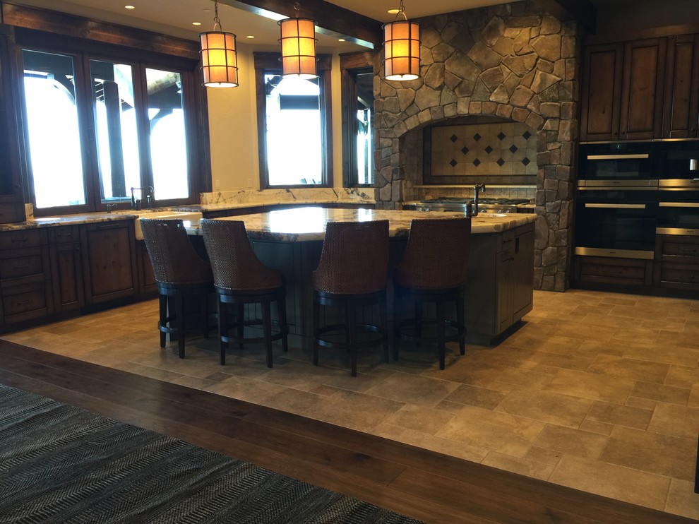 Inspiration for a large rustic u-shaped eat-in kitchen remodel in Seattle with a farmhouse sink, flat-panel cabinets, dark wood cabinets, gray backsplash, stone tile backsplash, stainless steel appliances and an island