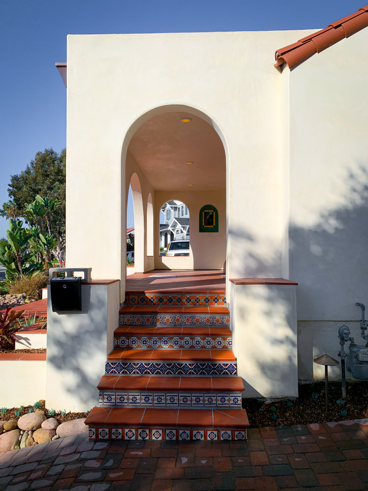 This is an example of a mid-sized mediterranean one-storey stucco white house exterior in San Diego with a gable roof and a tile roof.