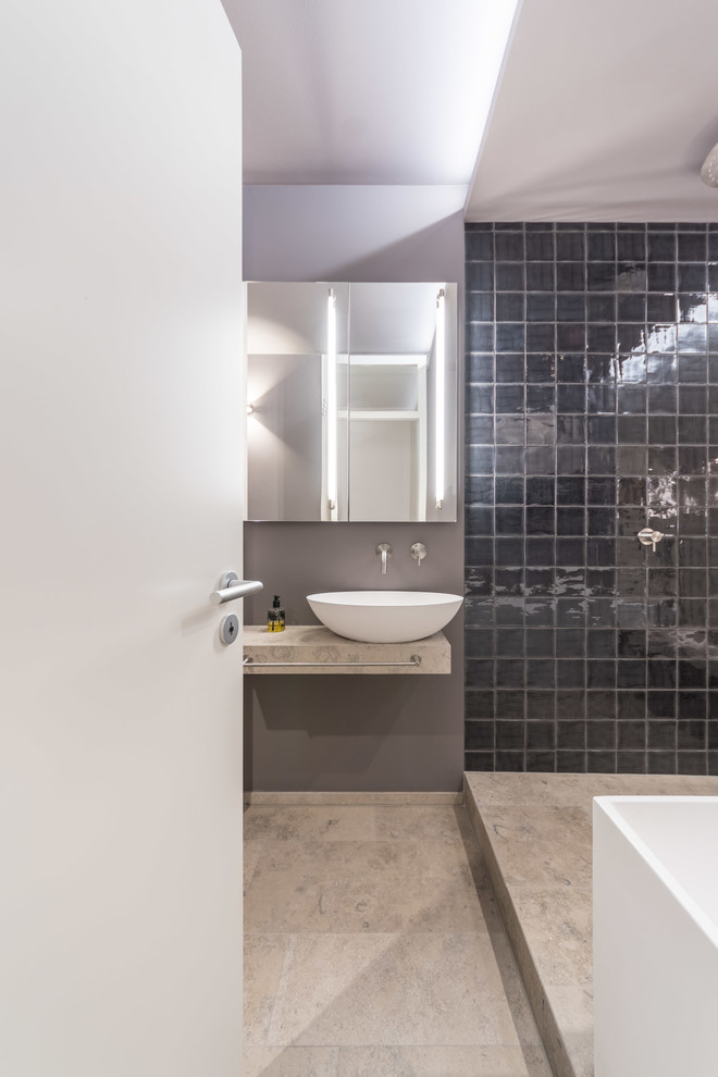 Duschbad mit flächenbündigen Schrankfronten, grauen Schränken, freistehender Badewanne, offener Dusche, Wandtoilette, schwarzen Fliesen, Keramikfliesen, grauer Wandfarbe, Kalkstein, Aufsatzwaschbecken, Kalkstein-Waschbecken/Waschtisch und grauem Boden in Munich