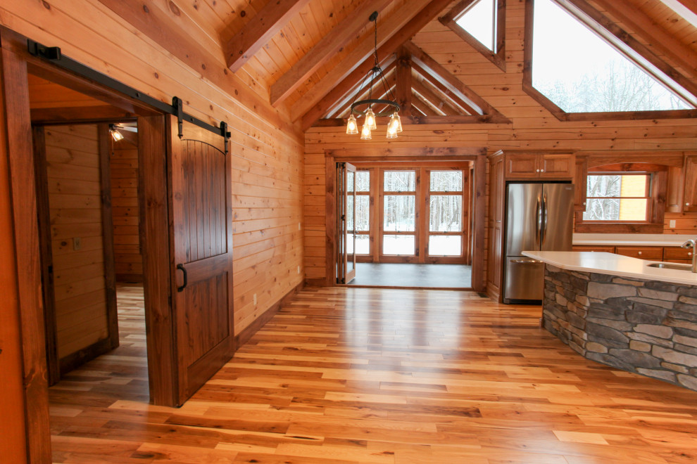 Mountain style u-shaped light wood floor, yellow floor and wood ceiling eat-in kitchen photo with a double-bowl sink, raised-panel cabinets, medium tone wood cabinets, wood backsplash, stainless steel appliances, an island and white countertops