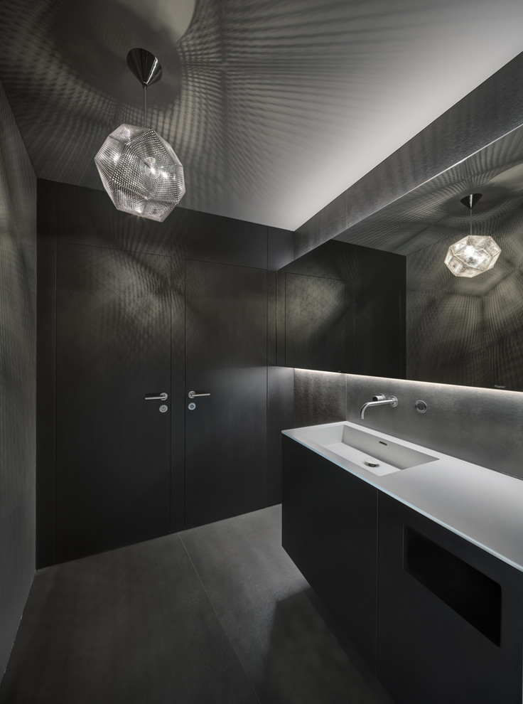 Badezimmer With flächenbündigen Schrankfronten, schwarzen Schränken, Wandtoilette, grauen Fliesen, Zementfliesen, grauer Wandfarbe, integriertem Waschbecken, Mineralwerkstoff-Waschtisch, grauem Boden and weißer Waschtischplatte in Munich