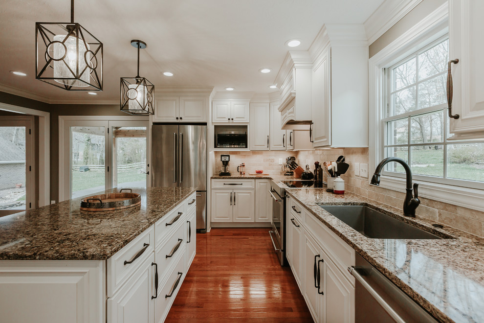 Inspiration for a mid-sized traditional l-shaped eat-in kitchen in Other with an undermount sink, raised-panel cabinets, white cabinets, granite benchtops, brown splashback, travertine splashback, stainless steel appliances, light hardwood floors, with island and brown benchtop.
