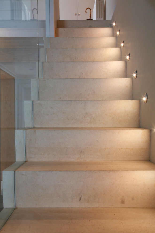 Diseño de escalera recta contemporánea con escalones de piedra caliza, contrahuellas de piedra caliza y barandilla de vidrio