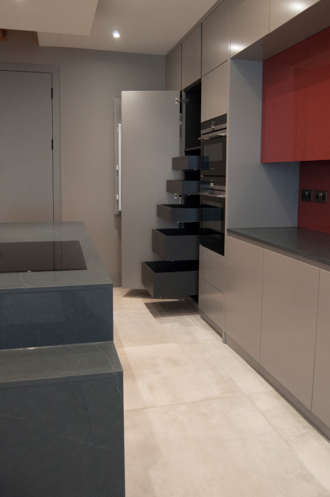 Photo of a large modern single-wall open plan kitchen in London with a double-bowl sink, flat-panel cabinets, grey cabinets, quartzite benchtops, red splashback, glass sheet splashback, black appliances, cement tiles, with island, grey floor and grey benchtop.