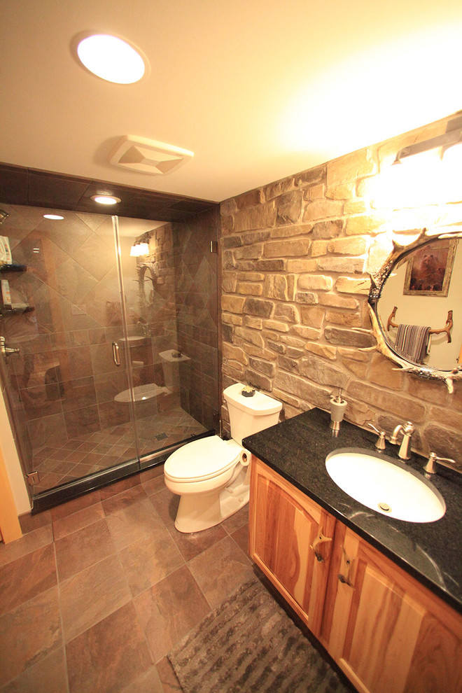 This is an example of a mid-sized country 3/4 bathroom in Philadelphia with raised-panel cabinets, medium wood cabinets, an alcove shower, a two-piece toilet, black tile, brown tile, gray tile, stone tile, grey walls, ceramic floors, an undermount sink and granite benchtops.