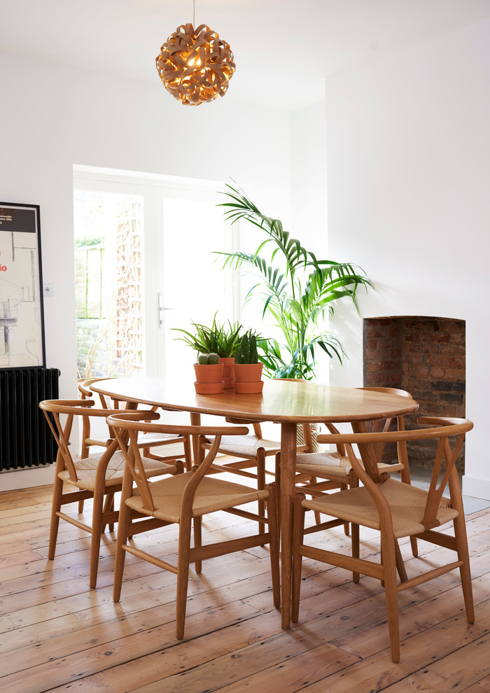 Photo of a mid-sized scandinavian open plan dining in London with white walls, medium hardwood floors, brown floor, a standard fireplace and a brick fireplace surround.