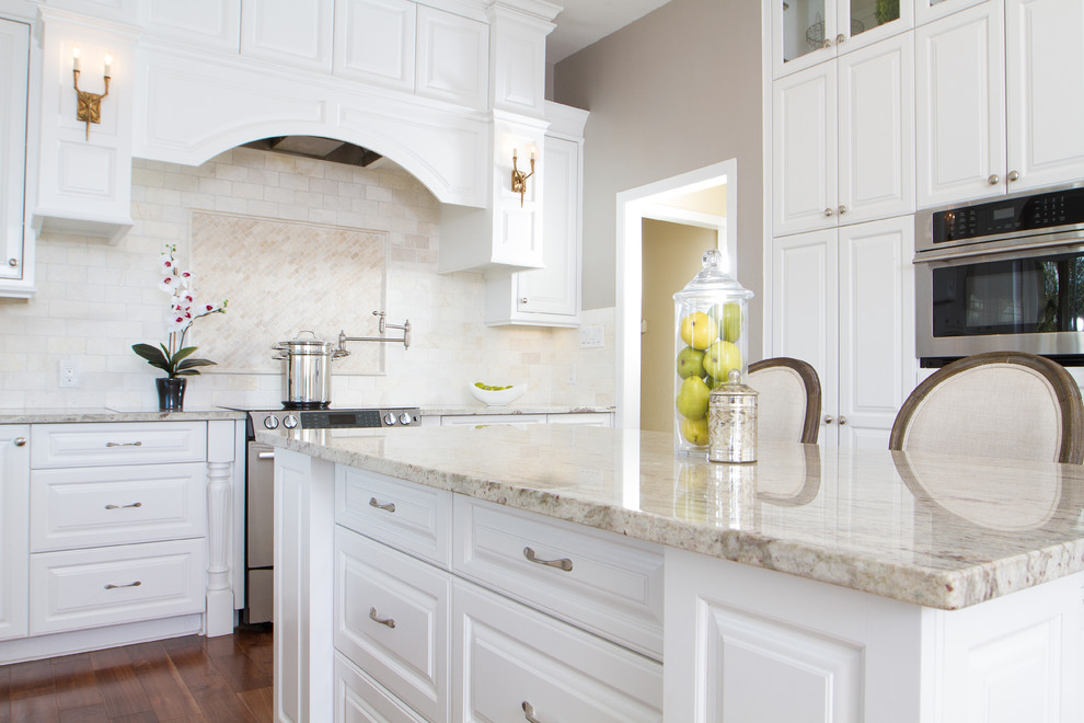 Example of a large transitional l-shaped medium tone wood floor eat-in kitchen design in Austin with a farmhouse sink, raised-panel cabinets, white cabinets, granite countertops, beige backsplash, ceramic backsplash, stainless steel appliances and an island