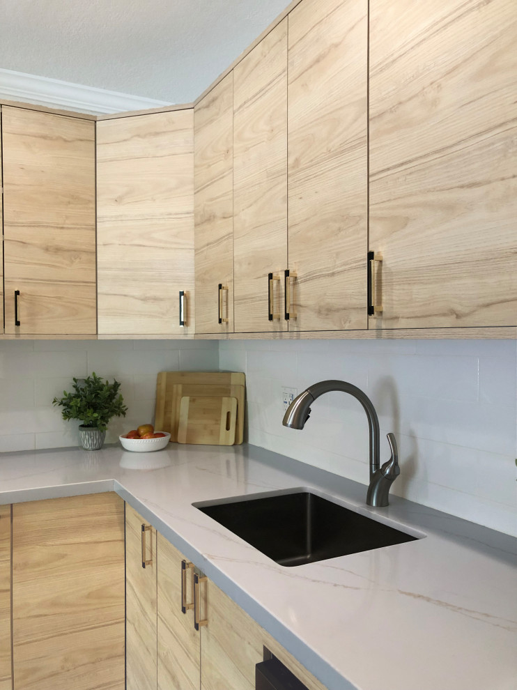 Photo of a small contemporary l-shaped eat-in kitchen in San Francisco with a single-bowl sink, flat-panel cabinets, light wood cabinets, quartzite benchtops, white splashback, subway tile splashback, stainless steel appliances, vinyl floors and white benchtop.