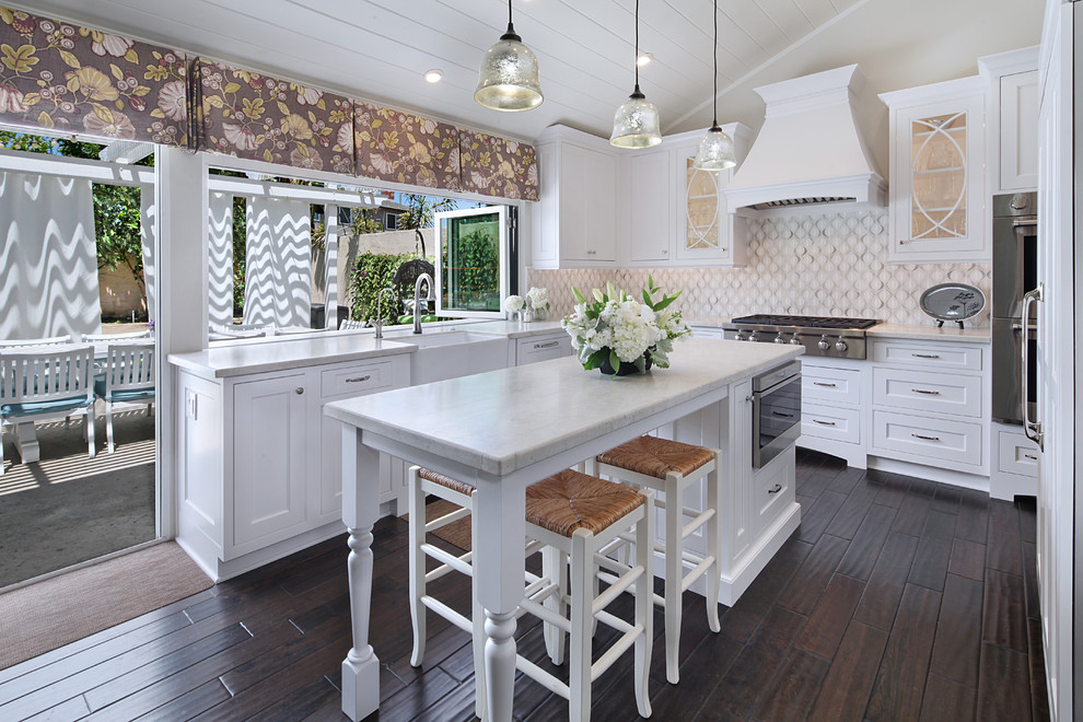 Enclosed kitchen - mid-sized transitional u-shaped dark wood floor enclosed kitchen idea in Orange County with a farmhouse sink, beaded inset cabinets, white cabinets, quartzite countertops, white backsplash, glass sheet backsplash, stainless steel appliances and an island