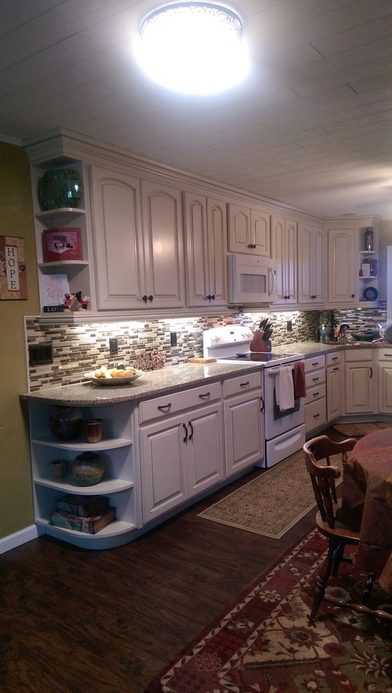 Example of a mid-sized transitional l-shaped laminate floor eat-in kitchen design with an undermount sink, raised-panel cabinets, white cabinets, granite countertops, multicolored backsplash, mosaic tile backsplash, white appliances and no island